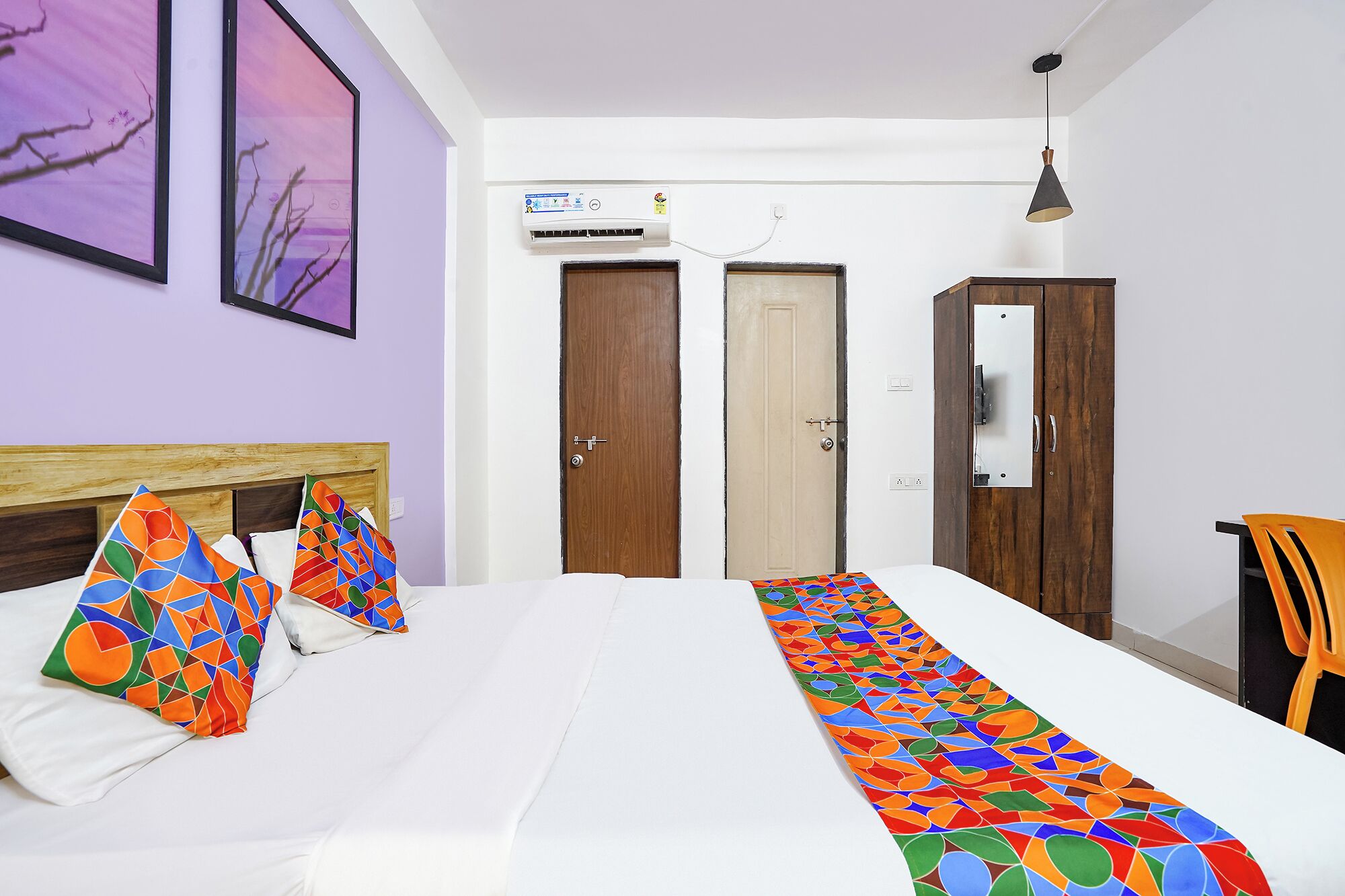 A hotel room with a bed, two doors, an air conditioning unit, a pendant light, and a chair.