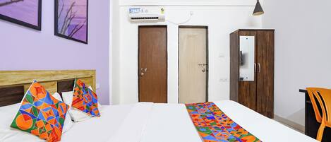 A hotel room with a bed, two doors, an air conditioning unit, a pendant light, and a chair.