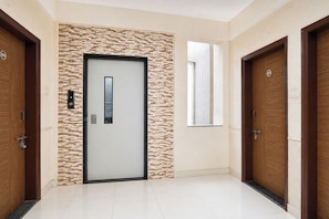 A hallway with a modern door featuring a digital display, a textured wall, and wooden doors on either side. - Fabhotel Noble Suites (Paud)