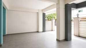 Un pasillo amplio con una puerta cerrada, suelo de baldosas y vista a un jardín a través de un espacio abierto.