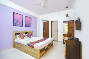 A bedroom with a bed, a desk, a chair, a ceiling fan, and two doors. - Fabhotel Noble Suites (Pune)