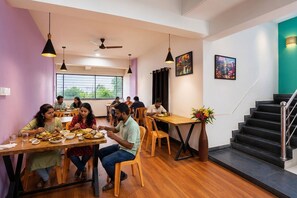 A dining area with tables, chairs, and people eating. There is a staircase and a wall with a picture. - Fabhotel Noble Suites (Paud)