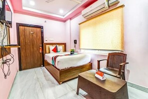 Habitación de hotel con una cama, una silla, una mesita, equipo de aire acondicionado y ventana con persiana.