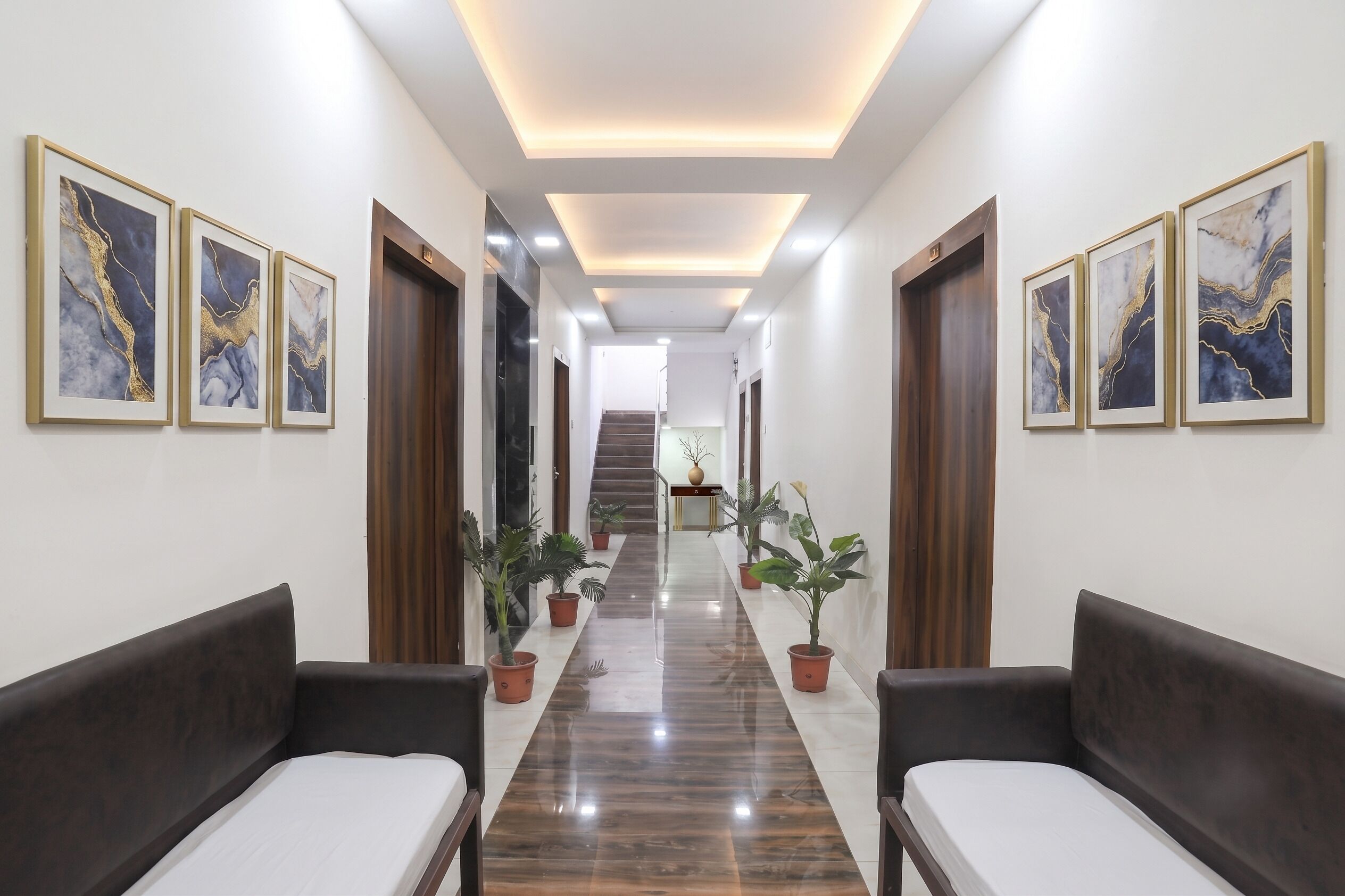 A hotel hallway with a central staircase, potted plants, and framed artwork on the walls.
