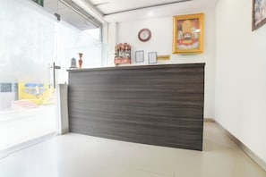 Un mostrador de recepción con acabado en madera oscura, un reloj, certificados enmarcados y una estatua religiosa en la pared.