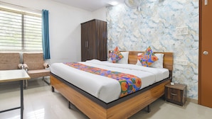 A bedroom with a bed, a bench, a wardrobe, and a wall-mounted fan. - FabHotel Manjulam Regency (Indore)