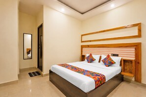 A hotel room with a large bed, a wooden headboard, a mirror, and a digital clock on the wall. - Fabhotel Green City Comforts (Bangalore)