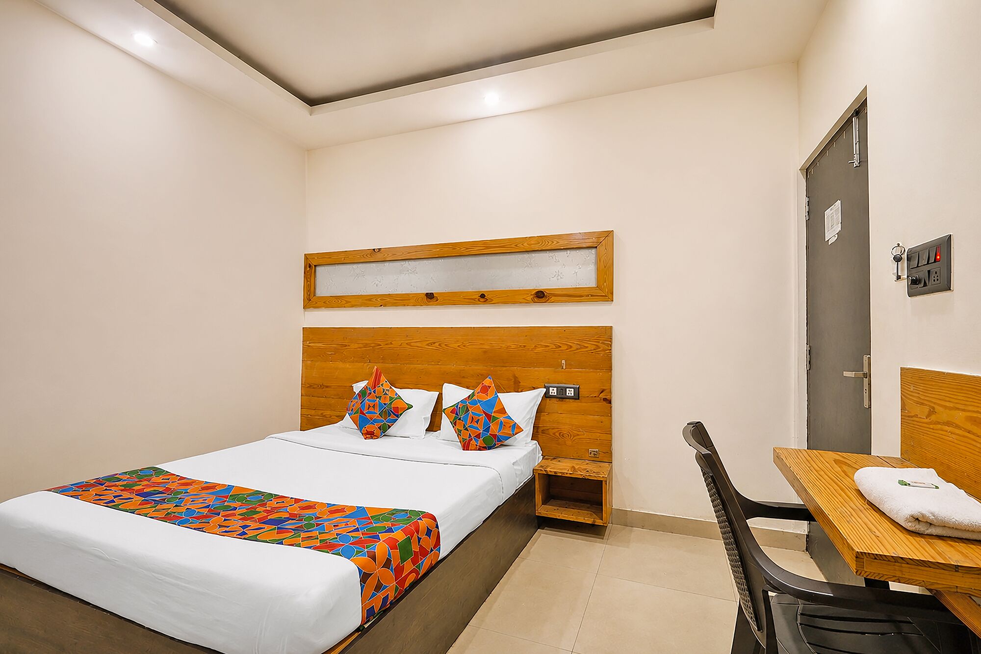 A bedroom with a bed, a wooden headboard, a bedside table, a chair, and a door.