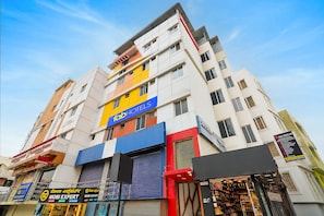 Un hotel de varios pisos con un llamativo letrero de 'Fab Hotels', una zona de recepción y diversas tiendas en la planta baja.