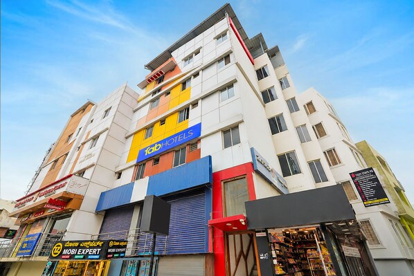 Un hôtel à plusieurs étages, reconnaissable à son grand panneau « Fab Hotels », doté d’un espace de réception et de différents commerces au rez-de-chaussée.