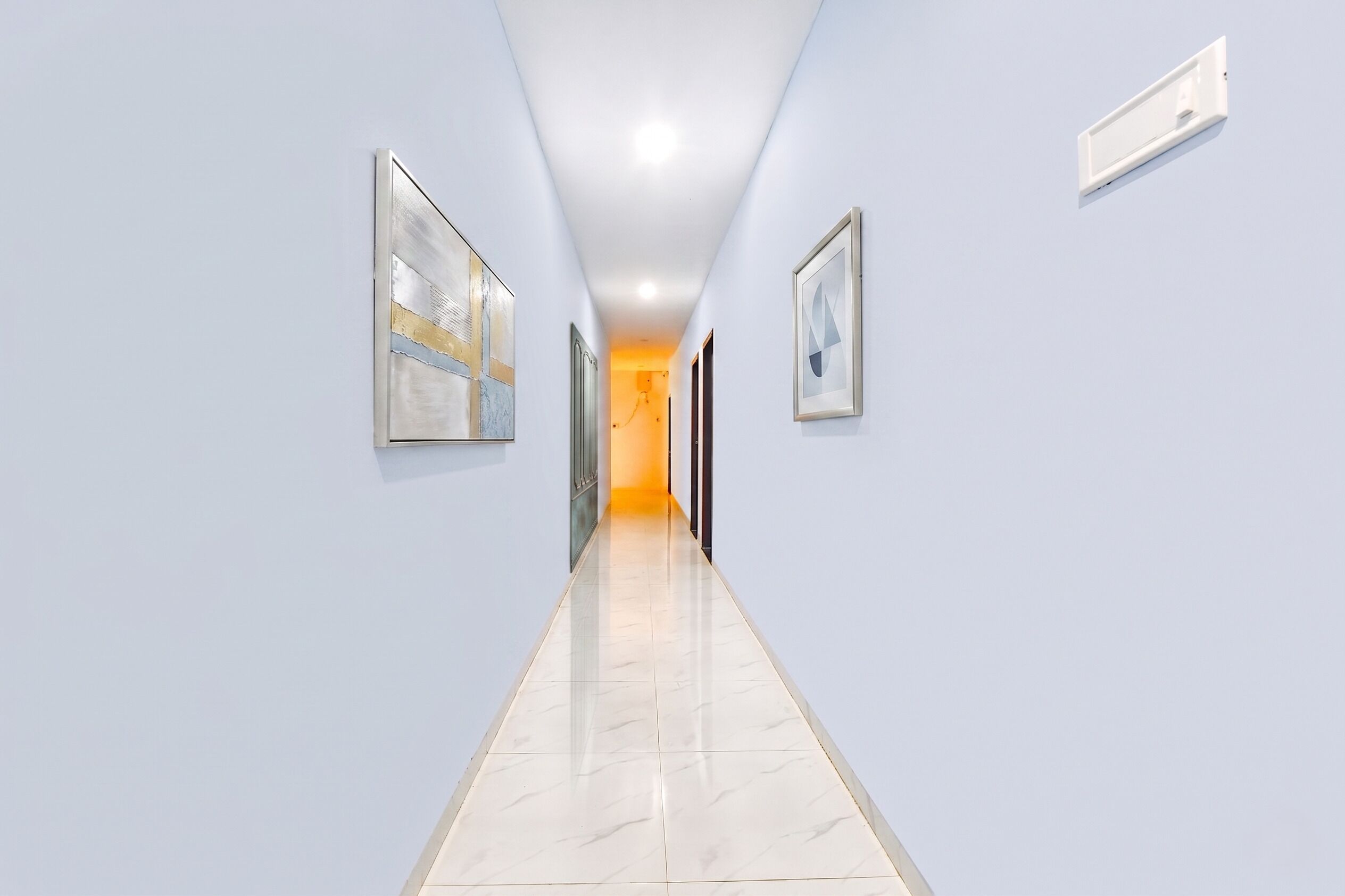 Un couloir aux murs bleu clair, doté d’un sol carrelé et orné d’œuvres d’art encadrées.