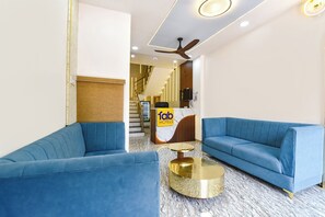 A hotel lobby with blue sofas, a reception desk, a ceiling fan, and a marble floor.