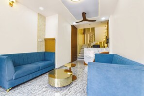A modern living room with blue sofas, a marble floor, a ceiling fan, and a staircase leading to a kitchen area. - FabHotel Shaurya Palace, Pithampur (Dhar)