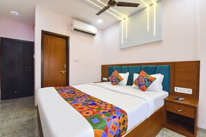 A hotel room with a bed, a nightstand, an air conditioning unit, a ceiling fan, and a door.