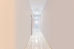 A corridor with white walls and a shiny floor, leading to a door with a red object on the wall.