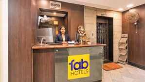 Ein Empfangsschalter mit einem 'Reception'-Schild, einem Computer, einem Ventilator und dem 'fab hotels'-Logo.