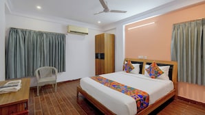 A hotel room with a bed, a chair, a desk, a ceiling fan, and an air conditioning unit. - FabHotel Prestige Lake Ridge - Nr Durgam Cheruvu Lake Front Park (Hyderabad)