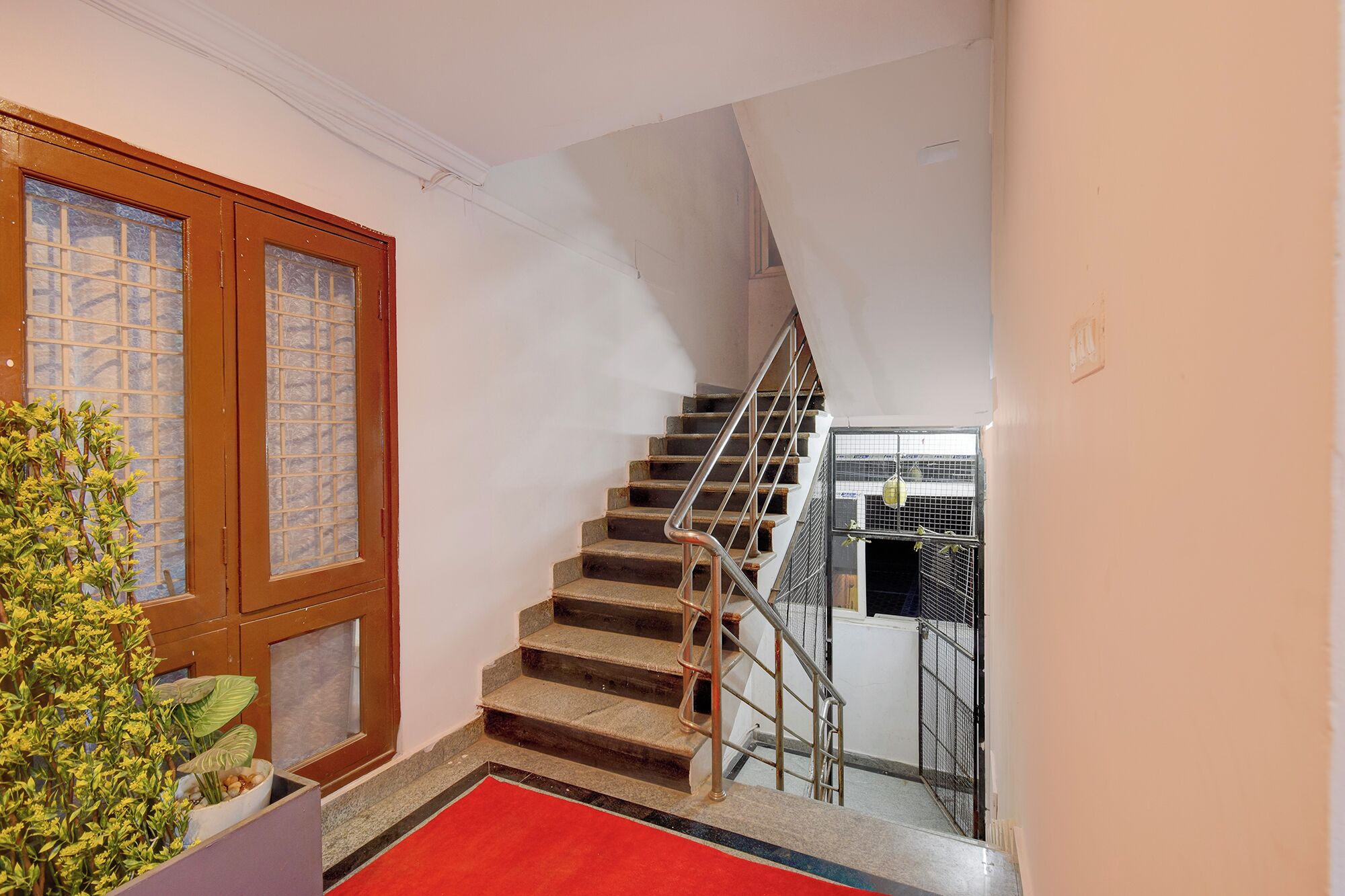 Una escala amb barana metàl·lica, un fermall vermell i una porta de fusta amb panells de vidre.