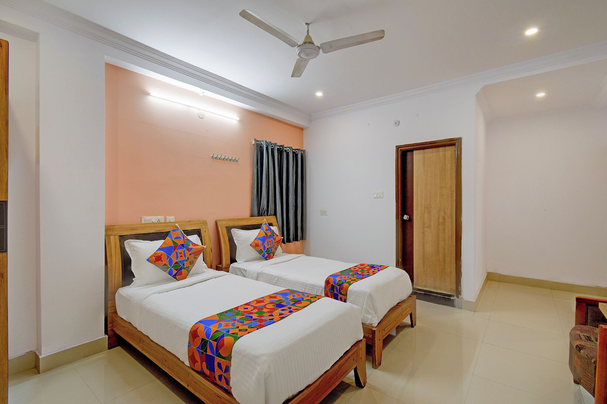 A hotel room with two beds, a ceiling fan, a door, and a light fixture.