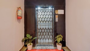 A hallway with a metal gate, two potted plants, a fire extinguisher, and a red mat. - FabHotel Prestige Lake Ridge - Nr Durgam Cheruvu Lake Front Park (Hyderabad)
