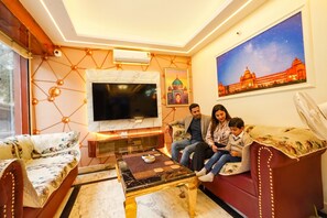 A living room with a TV, sofa, and a painting of a building. - FabHotel Bash - Nagarbhavi (Bangalore)