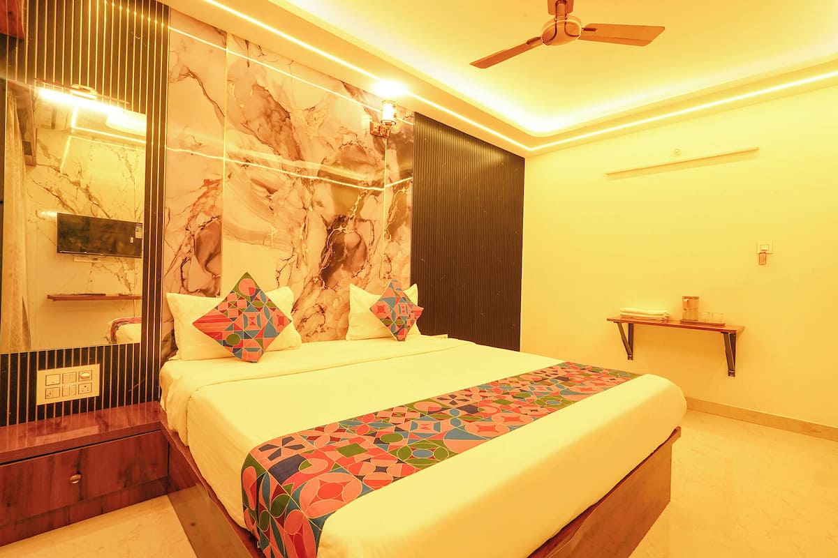 A bedroom with a bed, a ceiling fan, a TV, a bedside table, and a wall-mounted shelf.