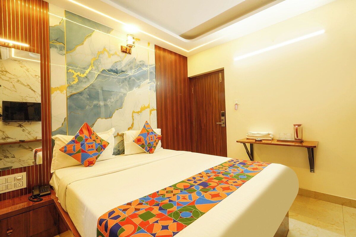 A hotel room with a bed, a bedside table, a TV, a wooden door, and a wall with a marble-like design.
