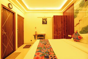 Quarto de hotel com uma cama, uma escrivaninha, uma cadeira e um relógio fixado na parede.