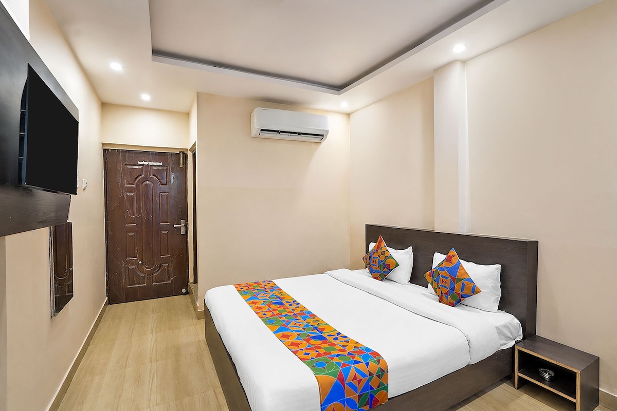 A hotel room with a bed, a TV, an air conditioning unit, and a wooden door.