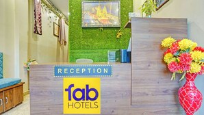 Un comptoir d’accueil avec une enseigne indiquant « fab hotels », un mur végétal agrémenté d’un tableau encadré et un vase rempli de fleurs.