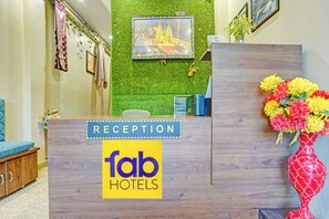 A reception desk with a 'fab hotels' sign, a green wall with a framed picture, and a vase of flowers. - Fahotel Rudransh Residency-1Km from Kashi Vishwanath Temple (Varanasi)