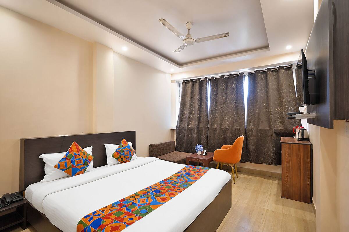Habitación de hotel con cama, escritorio, silla, televisor y ventilador de techo.