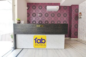 Uma mesa de recepção com o letreiro 'fab hotels', uma parede estampada e um aparelho de ar condicionado.