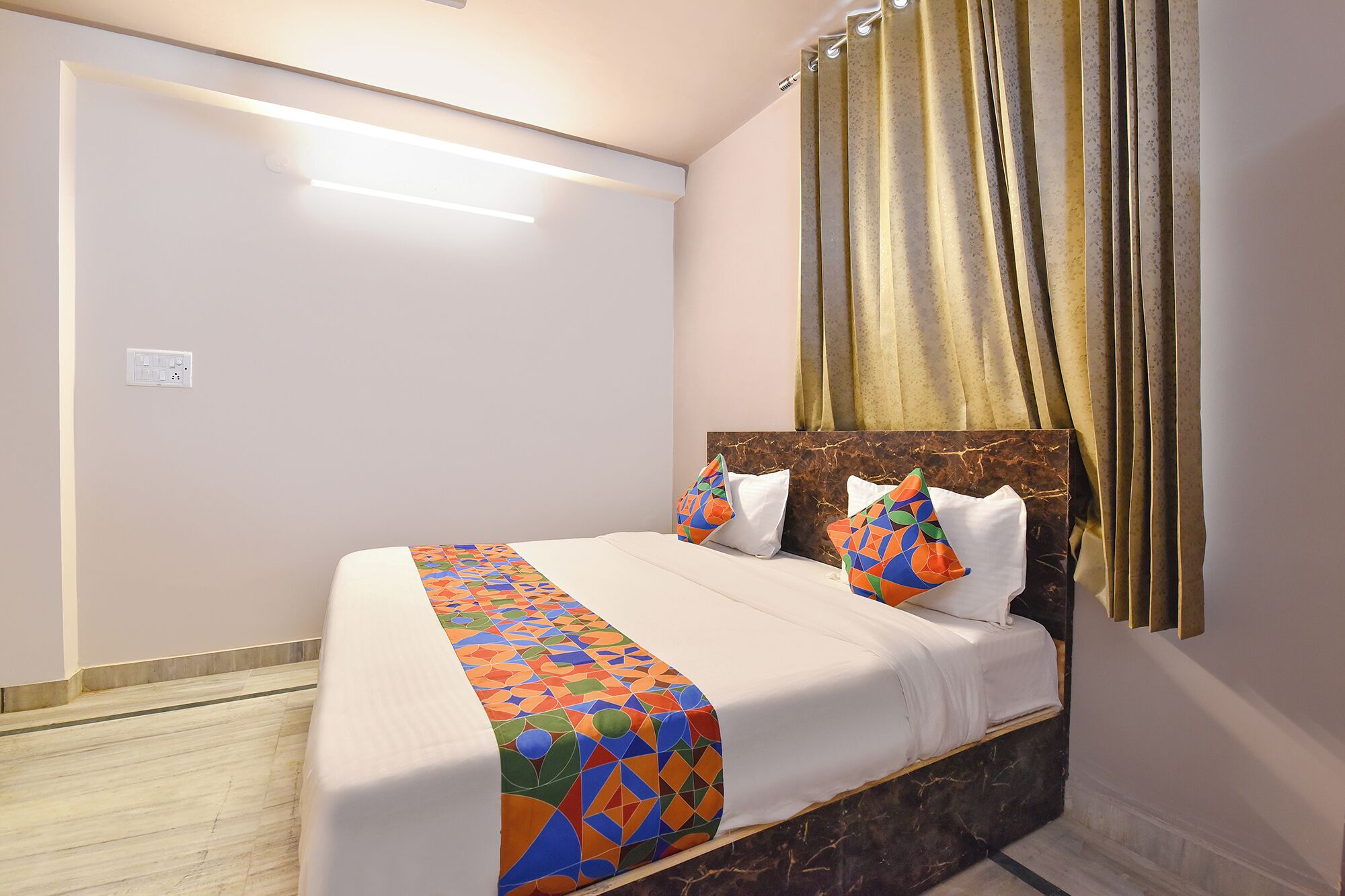 A hotel room with a bed, a marble headboard, a patterned bedspread, and a curtain.