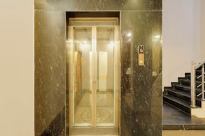 An elevator with a glass door, a metal handrail, and a stairway with a metal railing. - FabHotel Imperial (Varanasi)