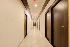 A long, narrow hotel corridor with doors on both sides, a tiled floor, and recessed ceiling lighting. - FabHotel Imperial (Varanasi)