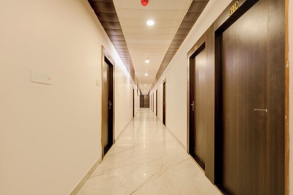 A long, narrow hotel corridor with doors on both sides, a tiled floor, and recessed ceiling lighting. - FabHotel Imperial (Varanasi)