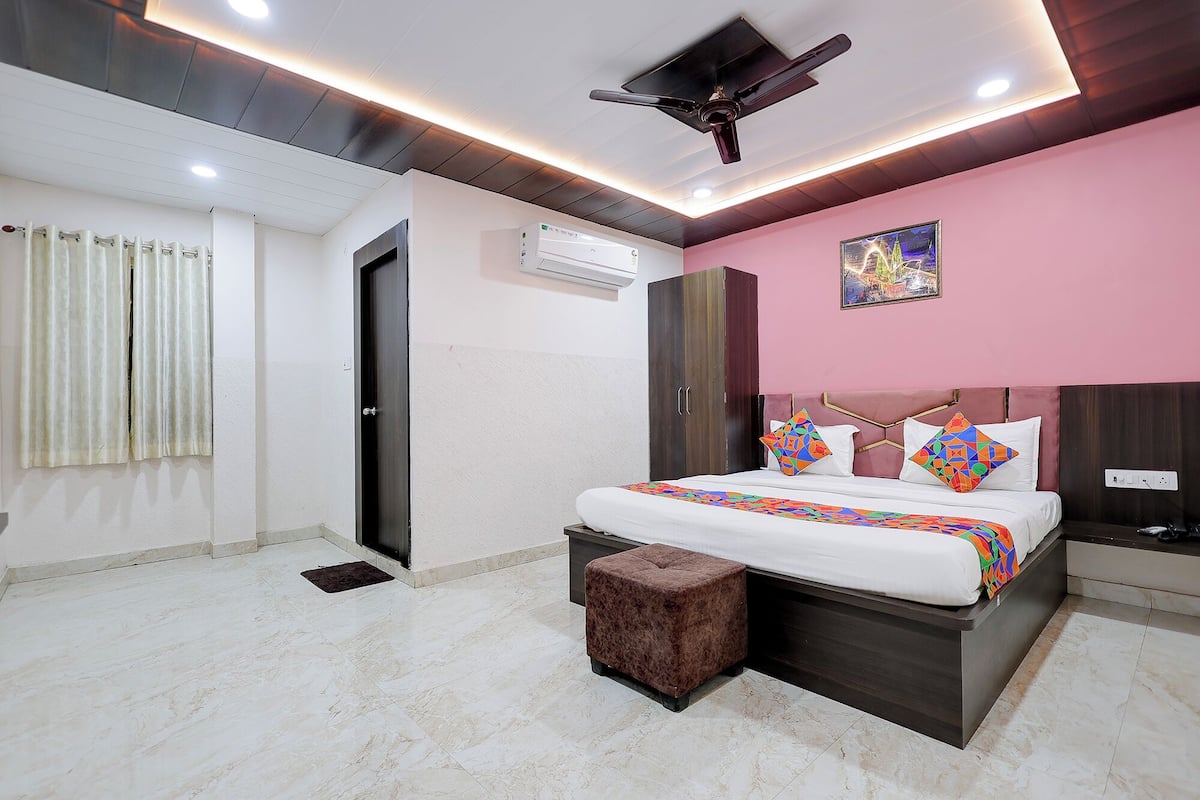 A bedroom with a bed, a ceiling fan, an air conditioning unit, a small stool, and a door.
