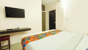 Quarto de hotel com cama, televisão na parede, escrivaninha e cadeira, além de uma porta.