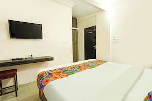 Quarto de hotel com cama, televisão na parede, escrivaninha e cadeira, além de uma porta.