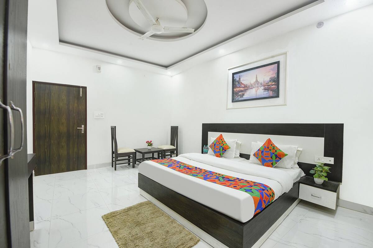 A modern bedroom with a bed, bedside table, chair, and a painting on the wall.