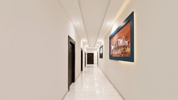 A hallway with a marble floor, framed artwork on the walls, and doors leading to rooms. - Fabhotel Rajvanshi Palace (Gurugram)
