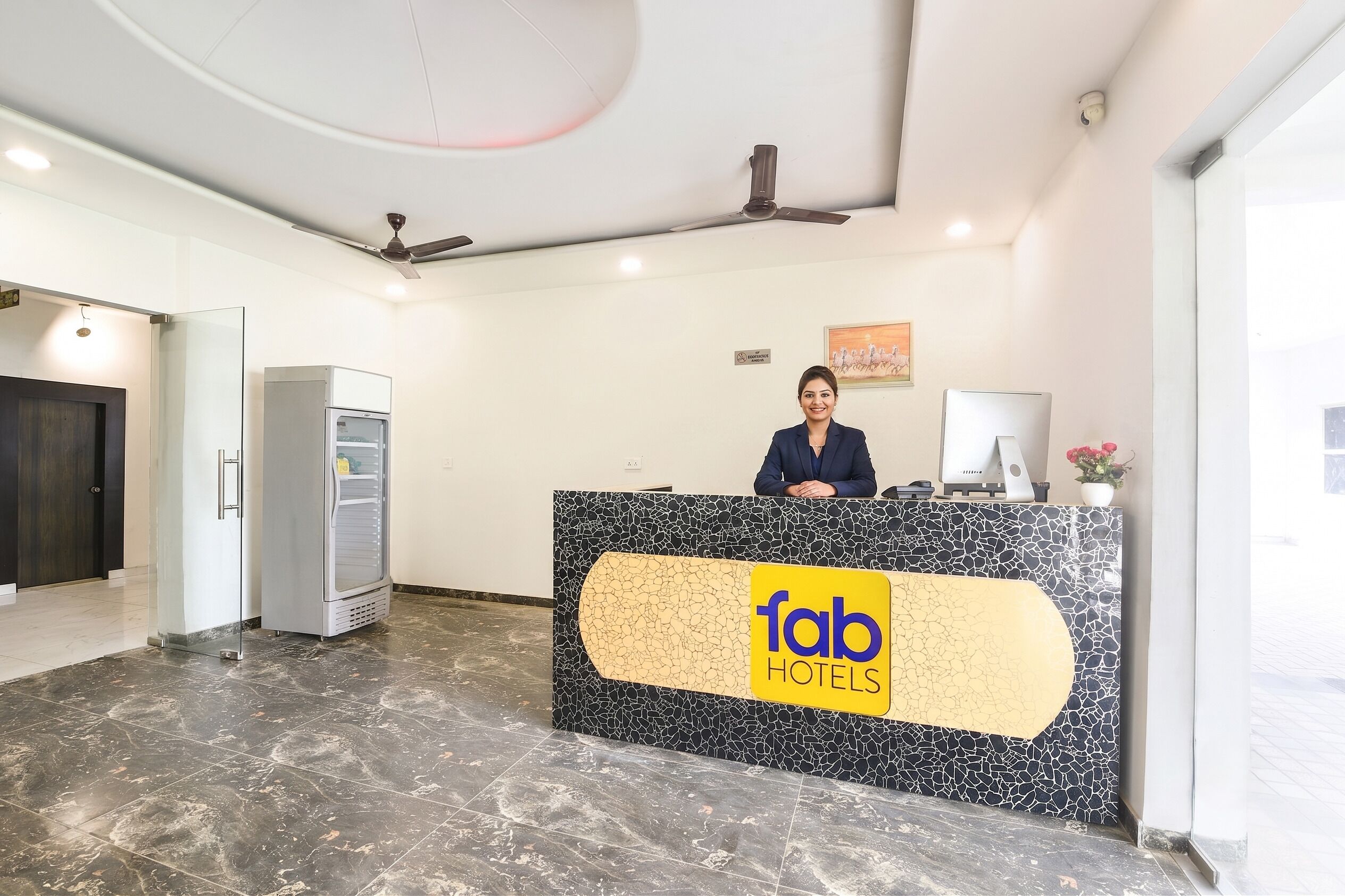 Un comptoir d’accueil avec un logo, un ventilateur de plafond, un réfrigérateur et une porte.