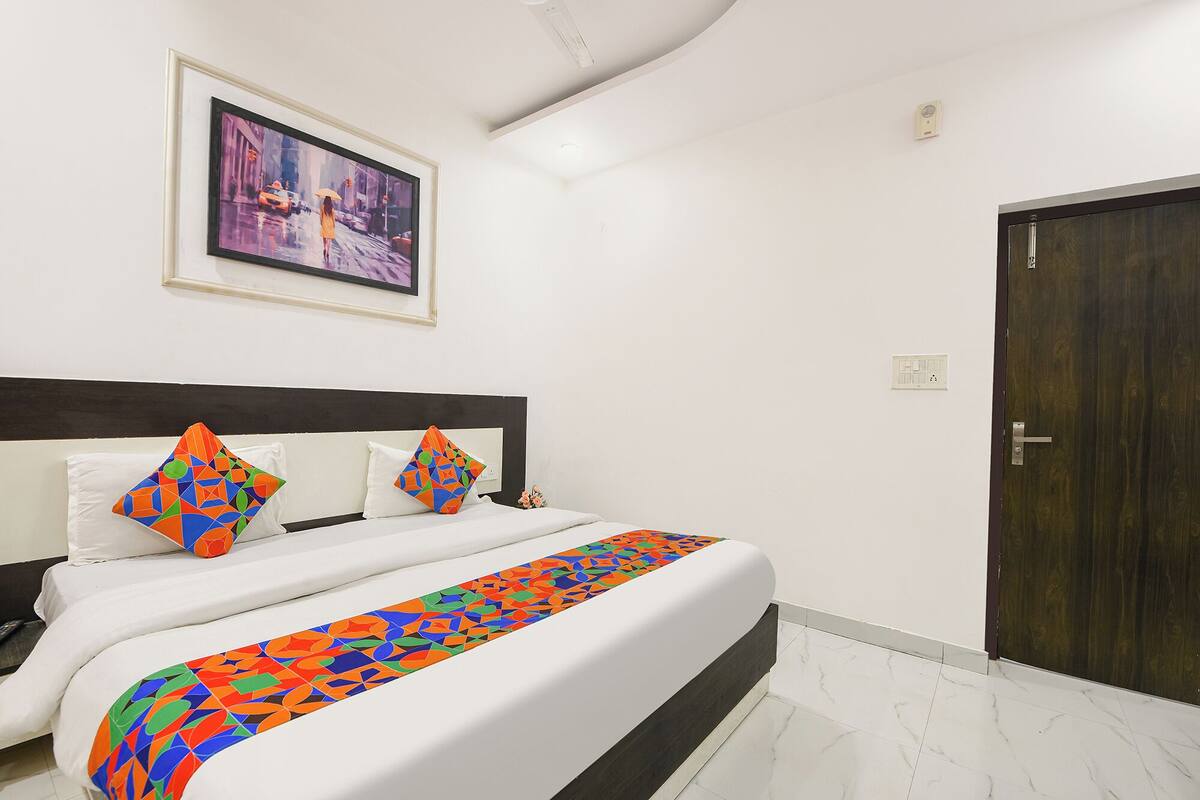 A hotel room with a bed, a framed picture on the wall, a door, and a light switch.