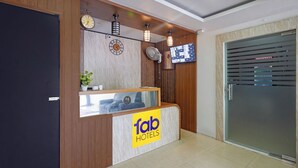 A hotel reception desk with a wooden finish, a clock, a TV screen, and a sign for 'Tap Hotels'. - Fabhotel Alfaa Inn (Bangalore)