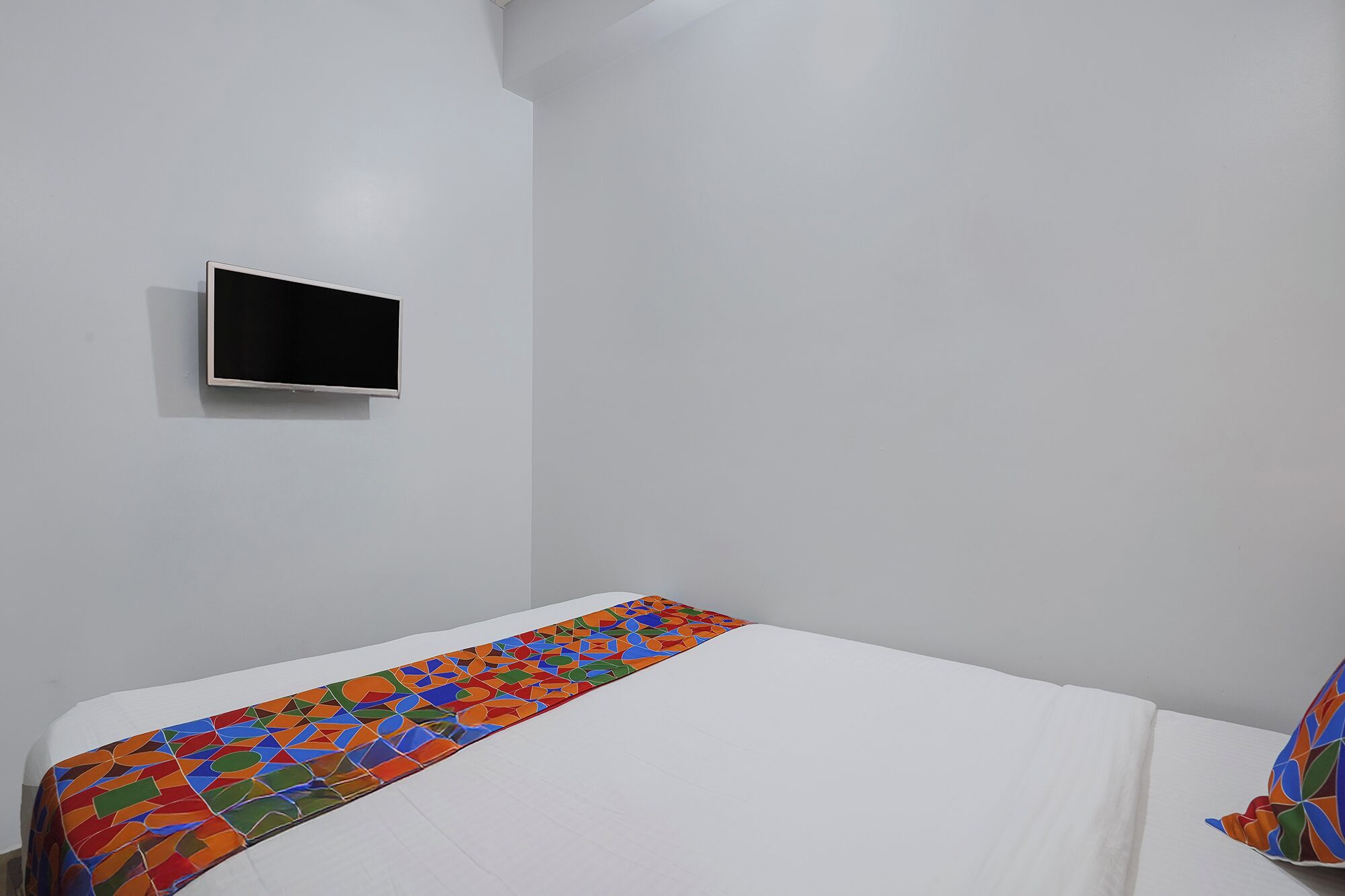 A room with a bed, a TV mounted on the wall, and a colorful geometric-patterned bedspread.