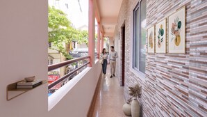 A corridor with a view of a street, a railing, and a wall with framed artwork. - Fabhotel Alfaa Inn (Bangalore)