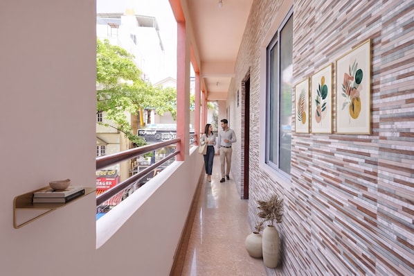 A corridor with a view of a street, a railing, and a wall with framed artwork.