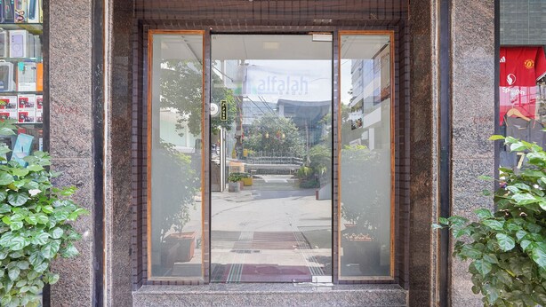 A building entrance with a glass door, a sign reading 'Alfalah Group,' and a small outdoor area with plants. - Fabhotel Alfaa Inn (Bangalore)