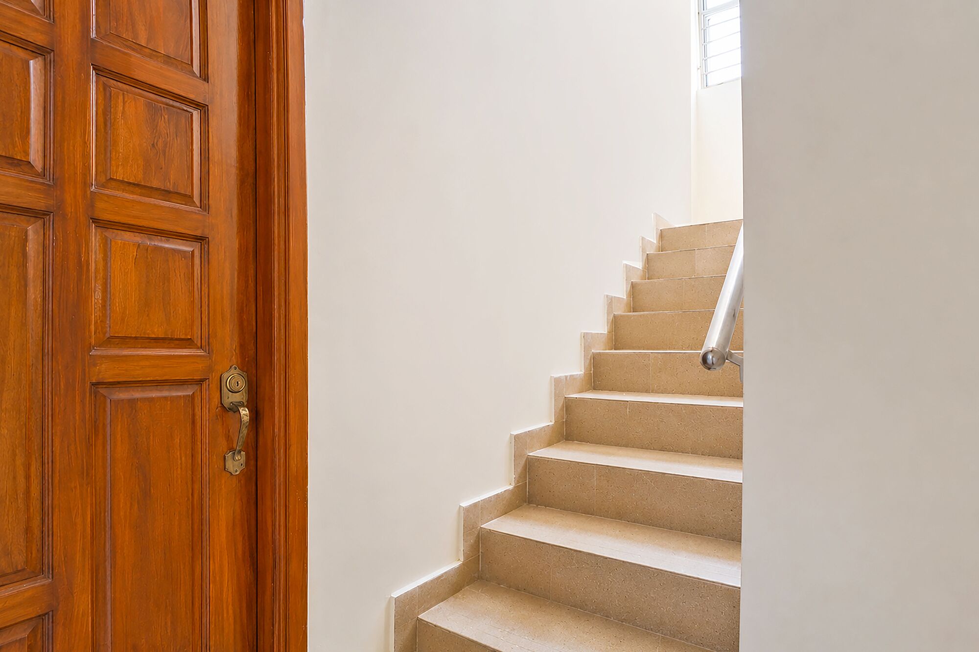 A wooden door with a brass handle, beige carpeted stairs, and a white wall.